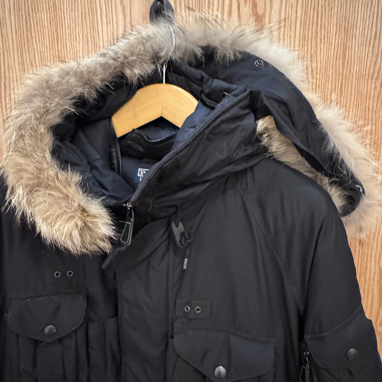 Black winter coat with fur-lined hood on a wooden hanger