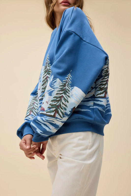 Blue sweater with a winter scene design worn by a person on a beige background