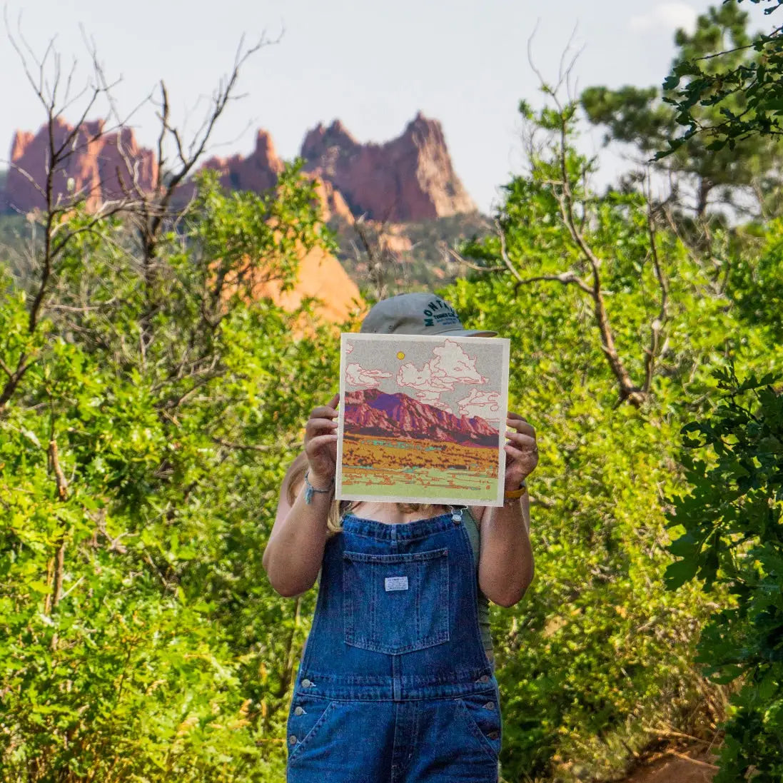 Person holding a print of a mountain scene in front of their face with a natural landscape in the background