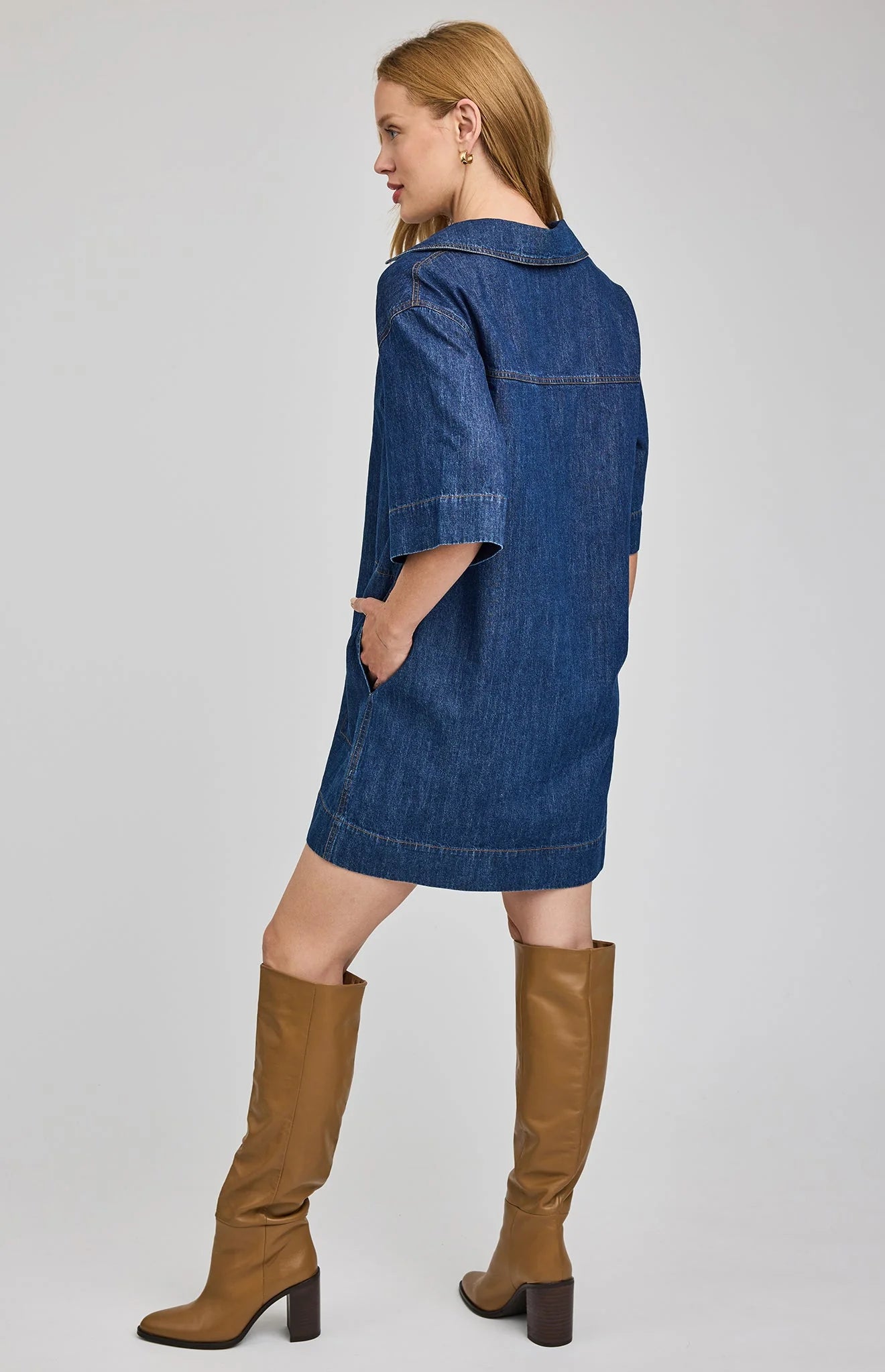 Woman wearing a blue denim dress and brown knee-high boots on a white background