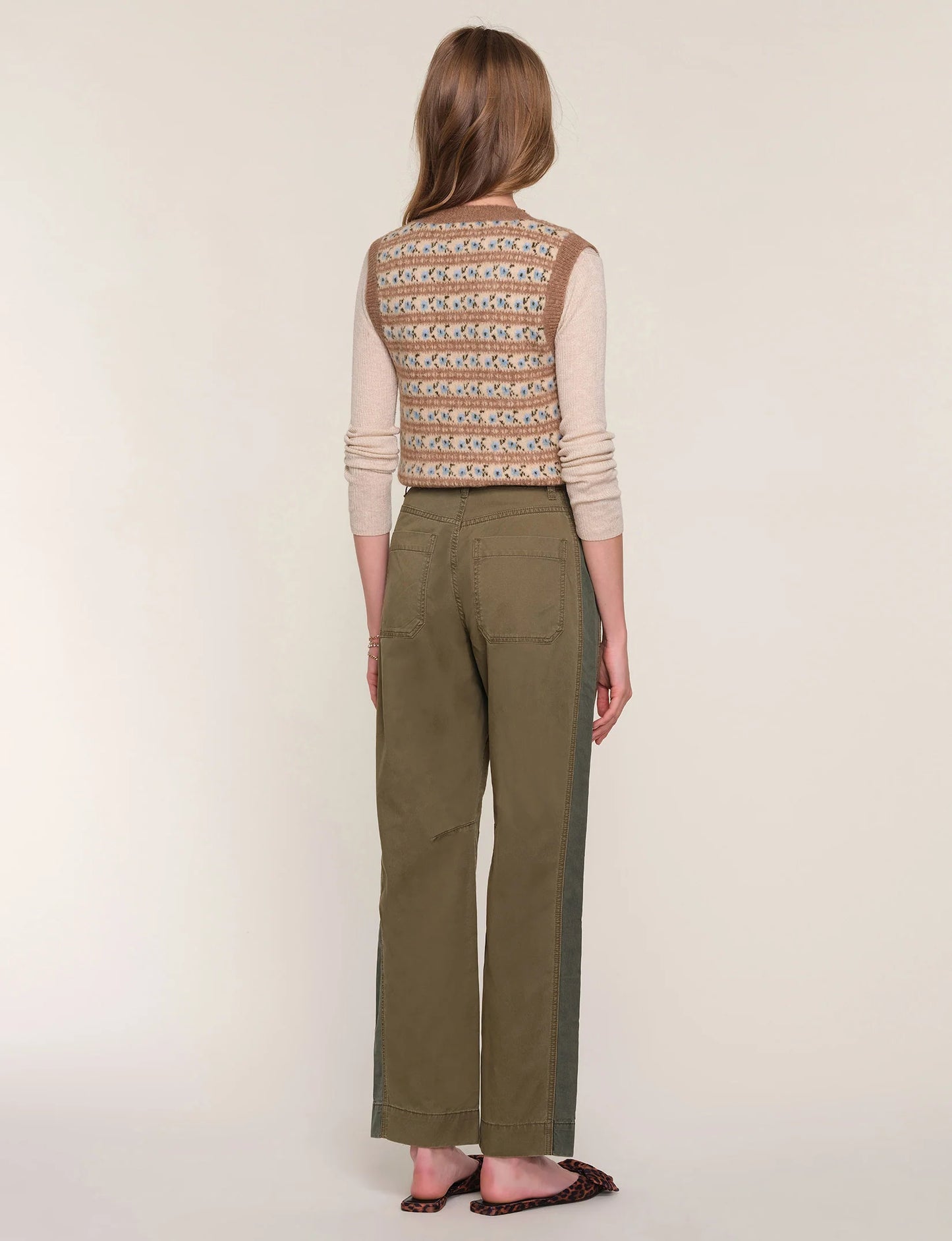 Woman wearing a patterned top and green pants on a white background