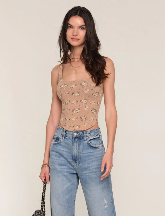 Woman wearing a beige floral tank top and blue jeans against a plain background