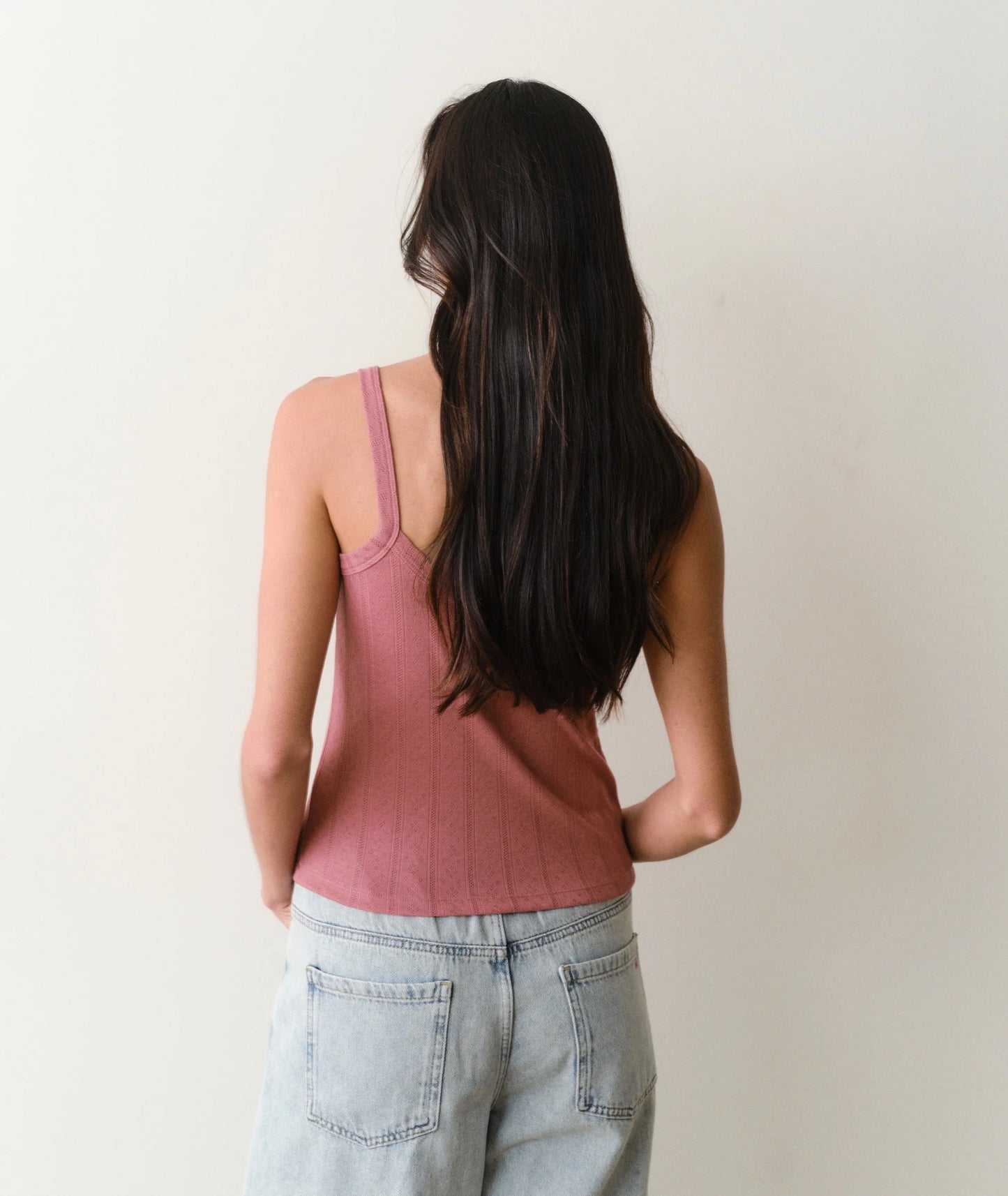 Person wearing a pink tank top and light blue jeans against a plain background