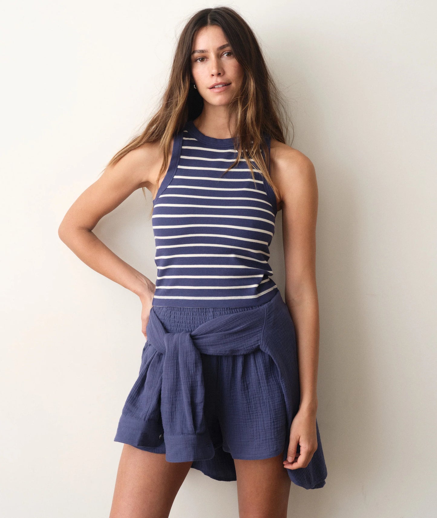 Woman wearing a blue and white striped top with a navy blue skirt against a plain background