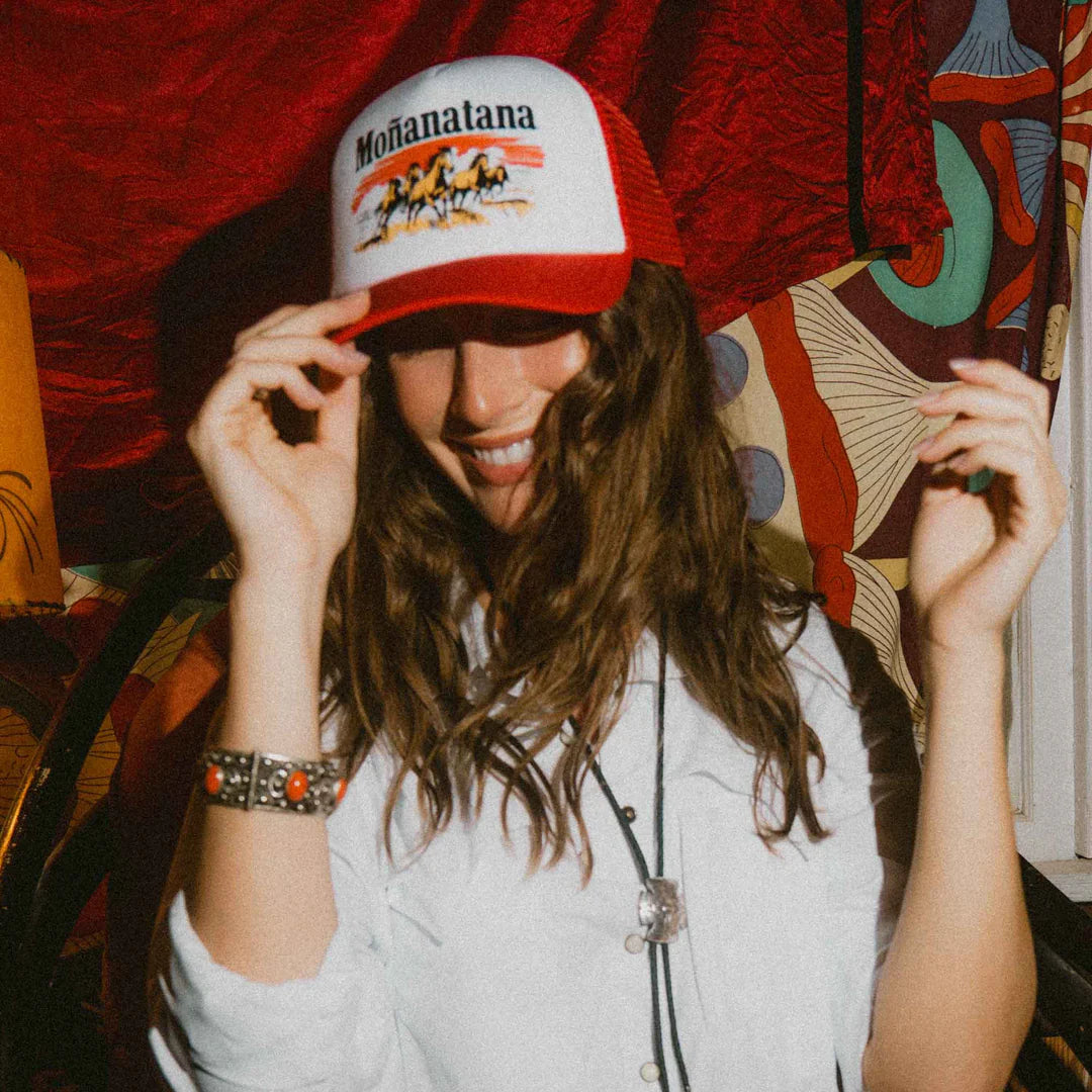 Person wearing a red and white cap with 'Mohanalana' branding, smiling in a colorful room.