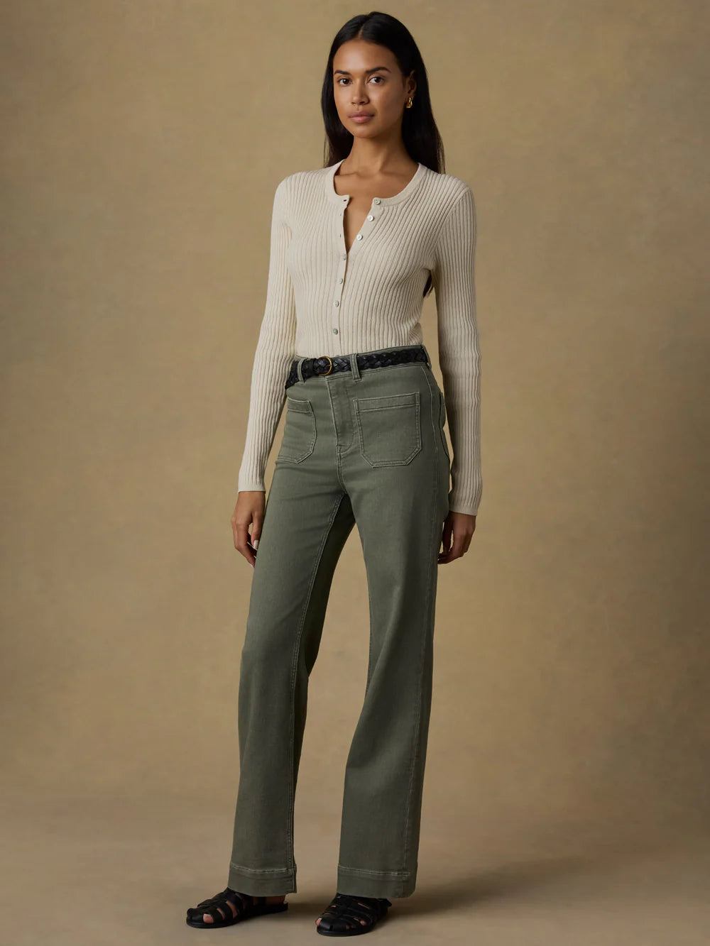 Woman wearing a white ribbed sweater and olive green pants against a beige background