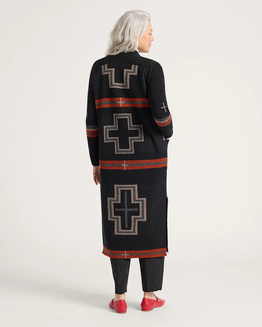 Person wearing a long black cardigan with geometric patterns on a white background