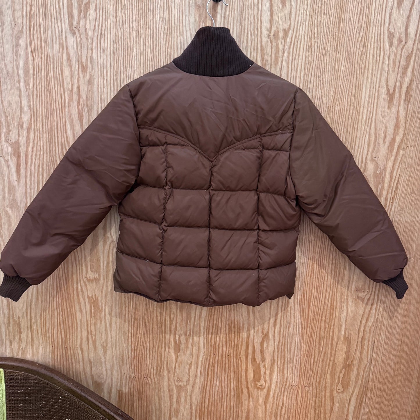 Brown puffer jacket on a hanger against a wooden background