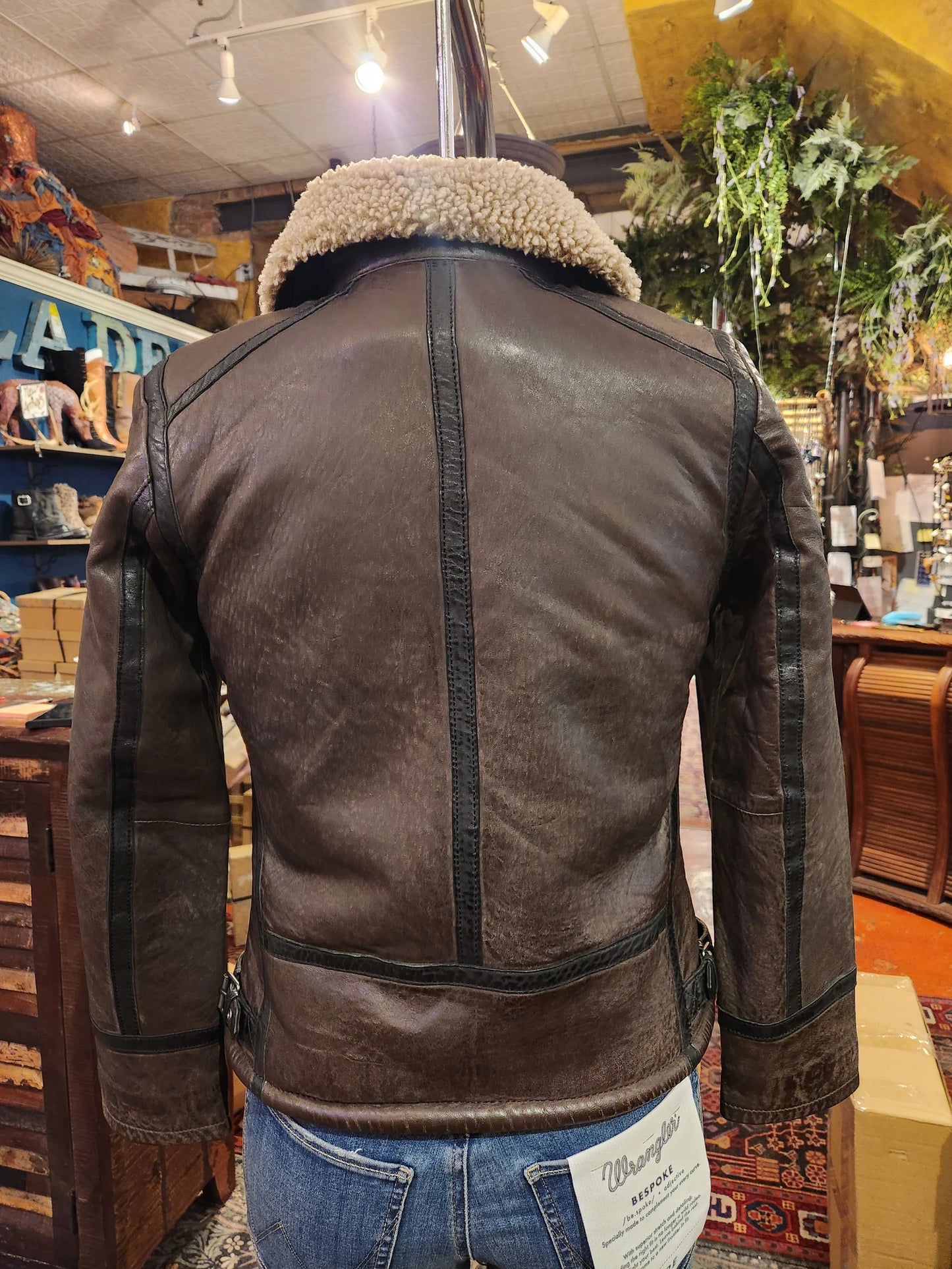 Brown leather jacket with sheepskin lining on a mannequin in a store setting.