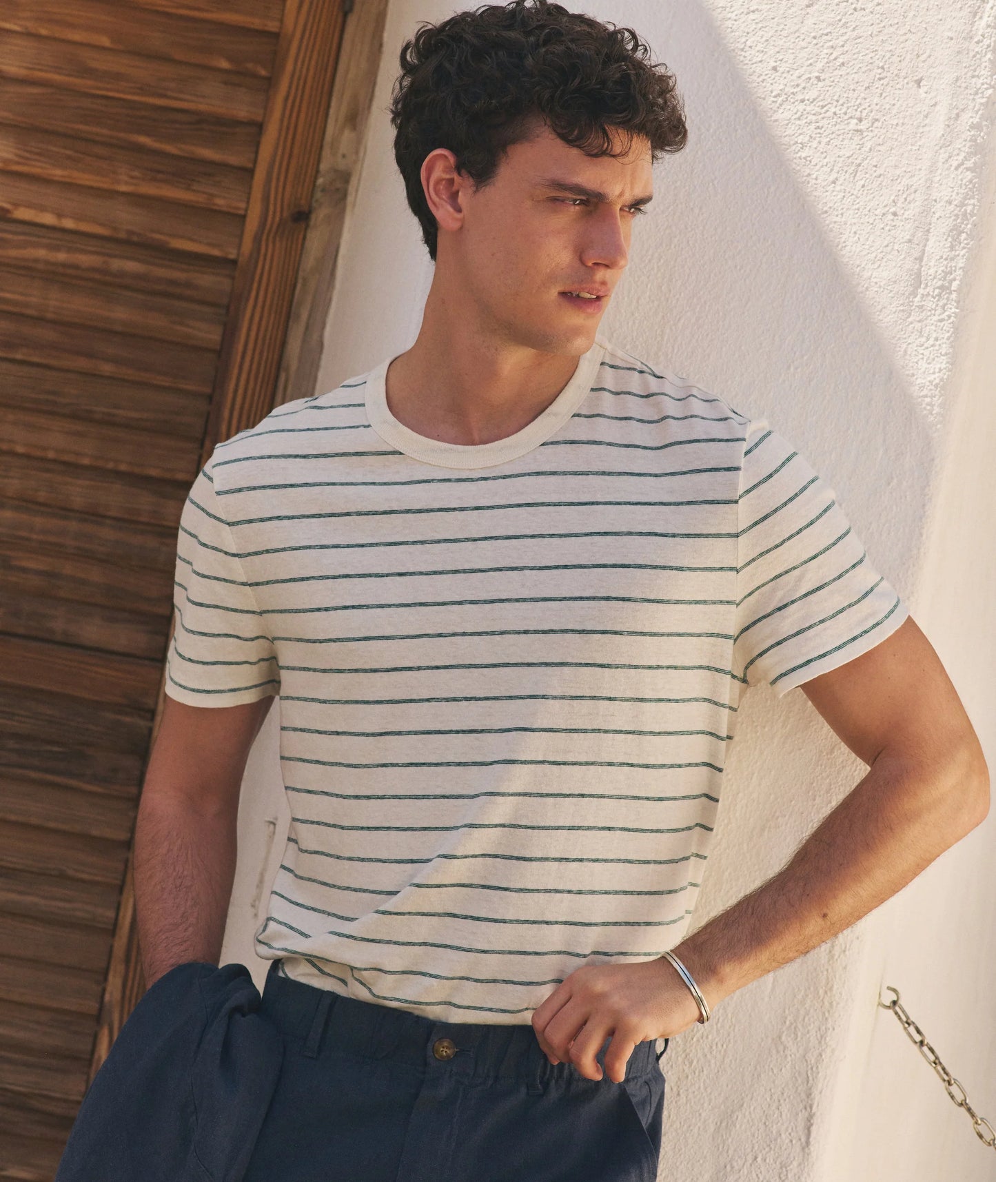 Man wearing a striped shirt leaning against a wooden wall.