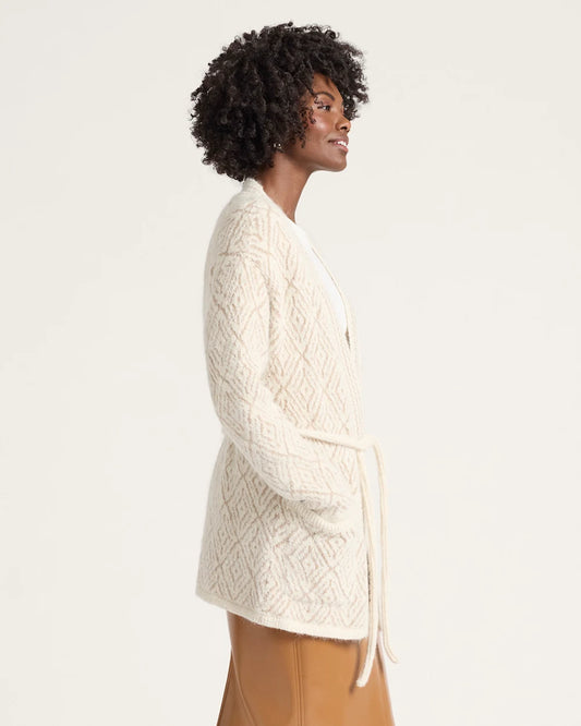 Woman wearing a cream-colored cable knit cardigan against a plain background