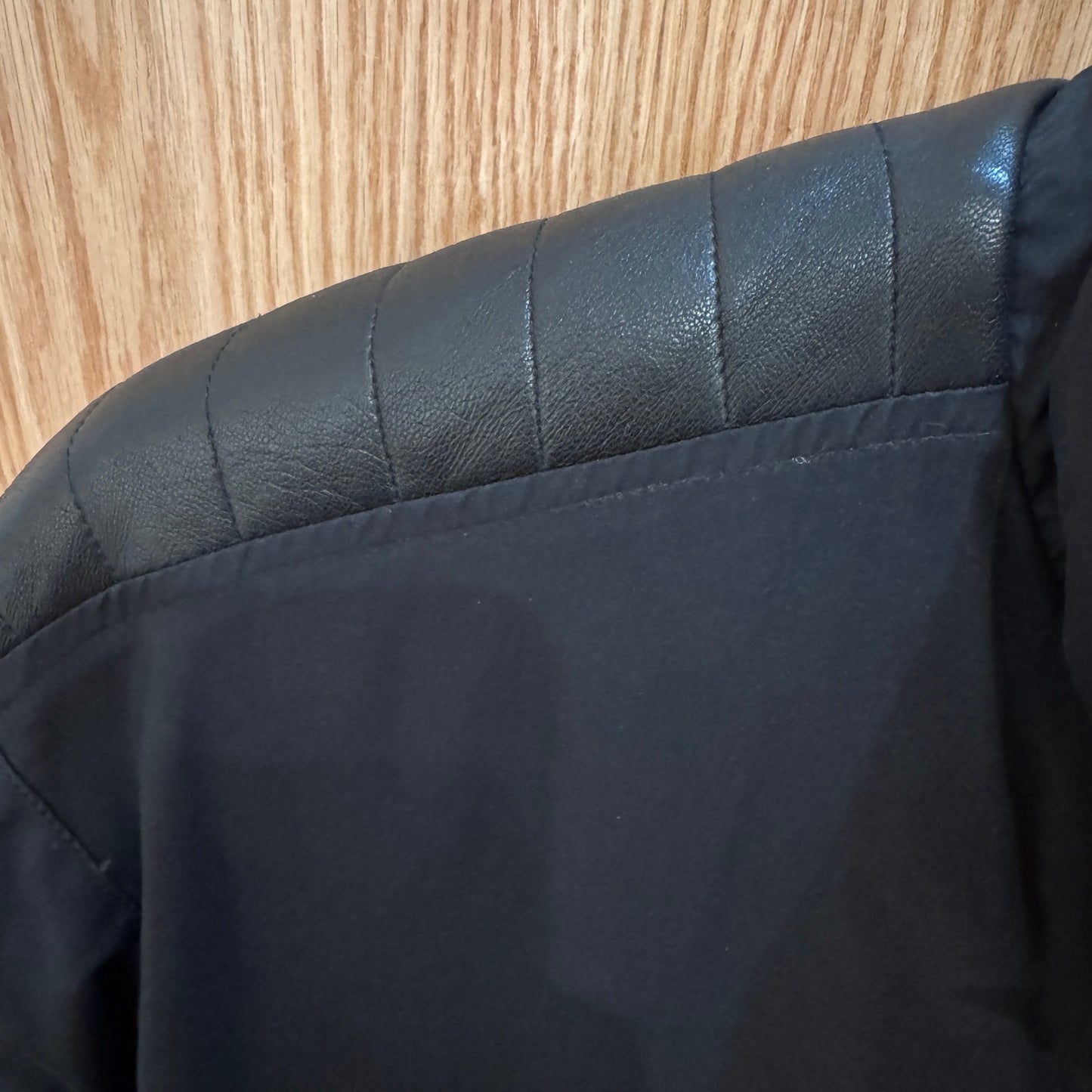 Close-up of a black jacket with quilted shoulder design on a wooden surface