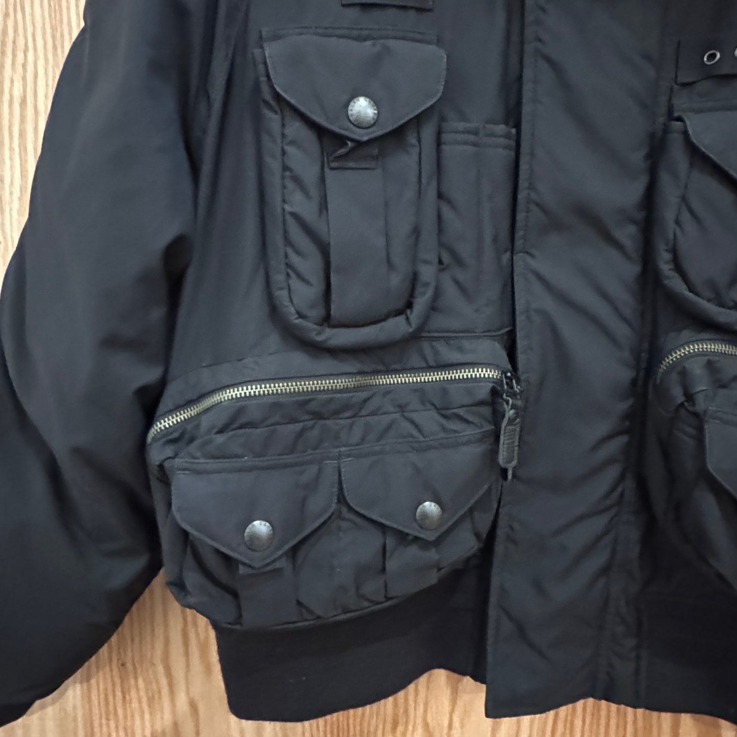 Black jacket with multiple pockets and zippers on a wooden surface