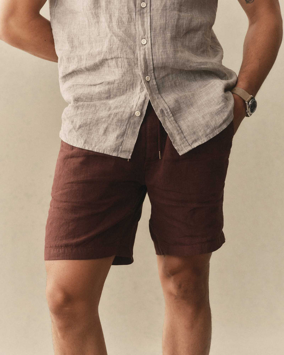 Person wearing a light-colored button-up shirt and maroon shorts on a neutral background