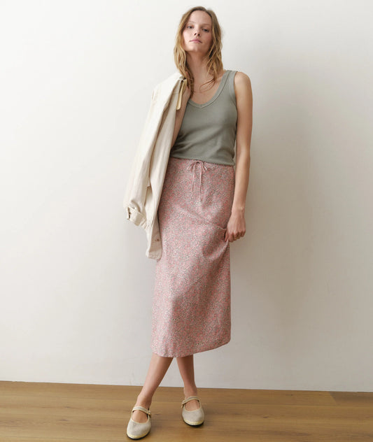 Woman wearing a green top and pink skirt against a white wall.