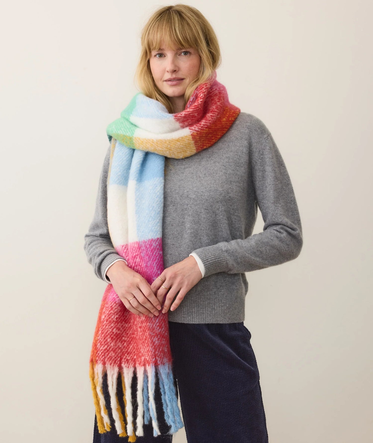 Woman wearing a colorful scarf and gray sweater against a plain background