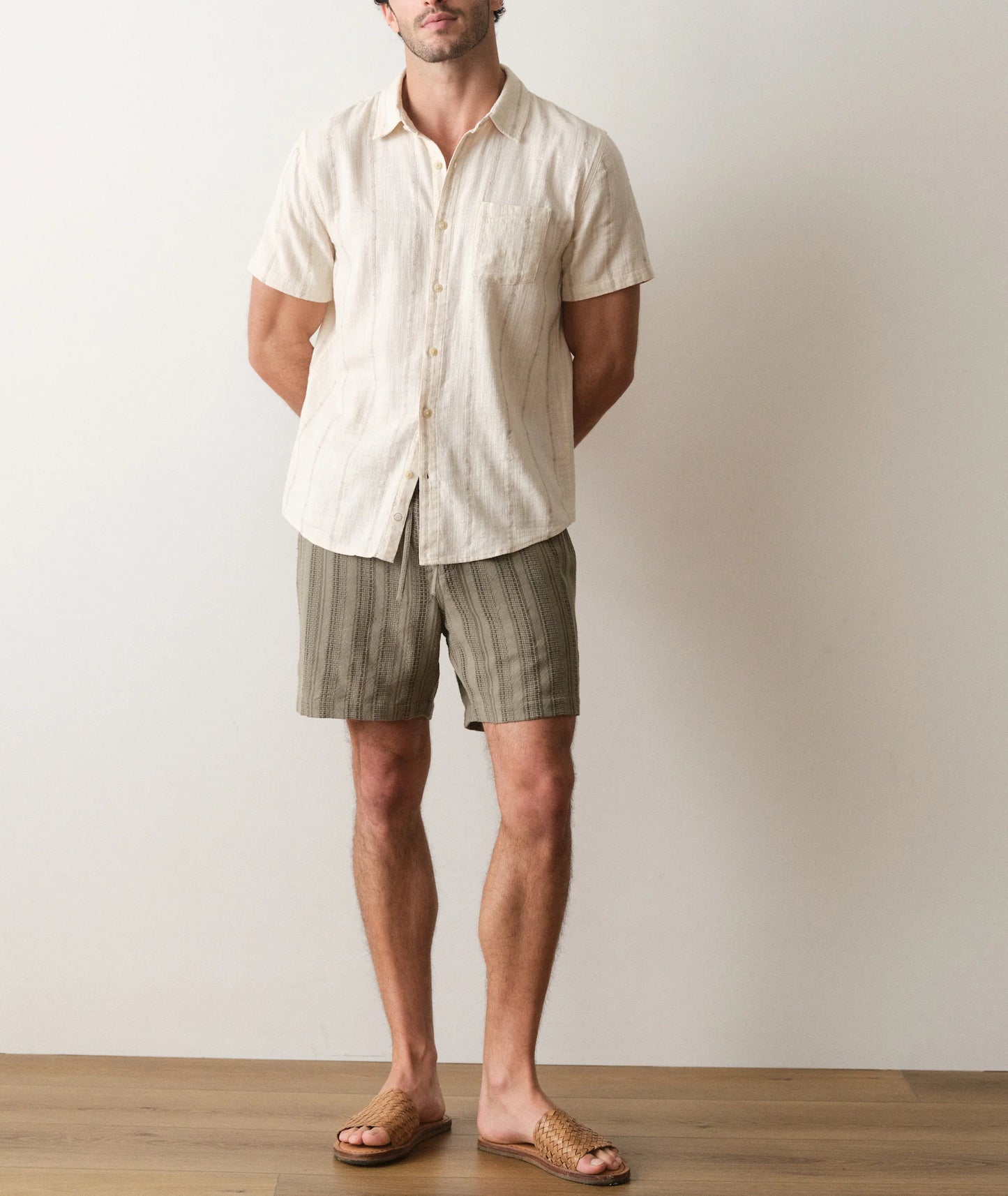 Man wearing a light-colored shirt and striped shorts standing against a plain background