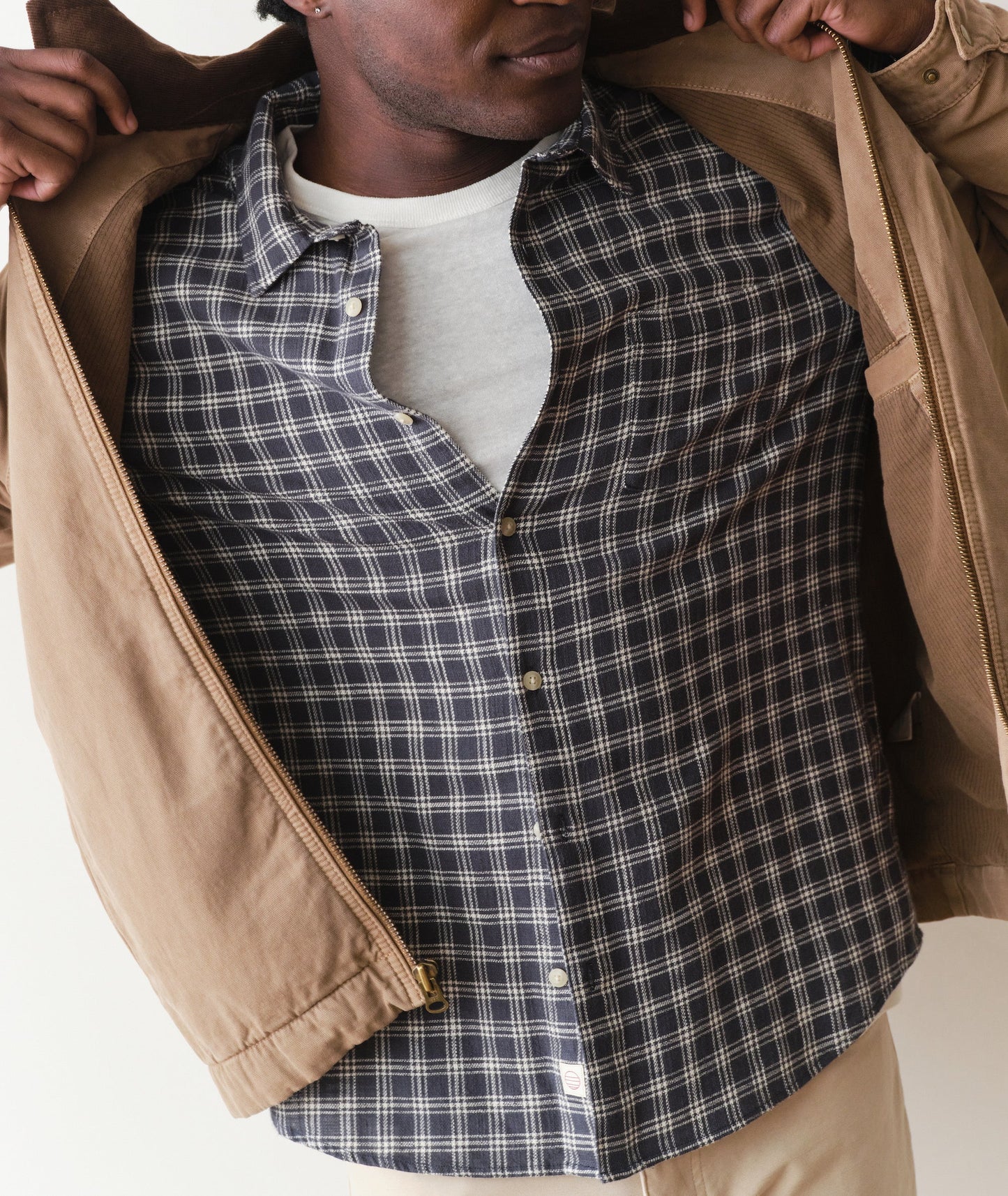 Person wearing a plaid shirt with a beige jacket on a white background