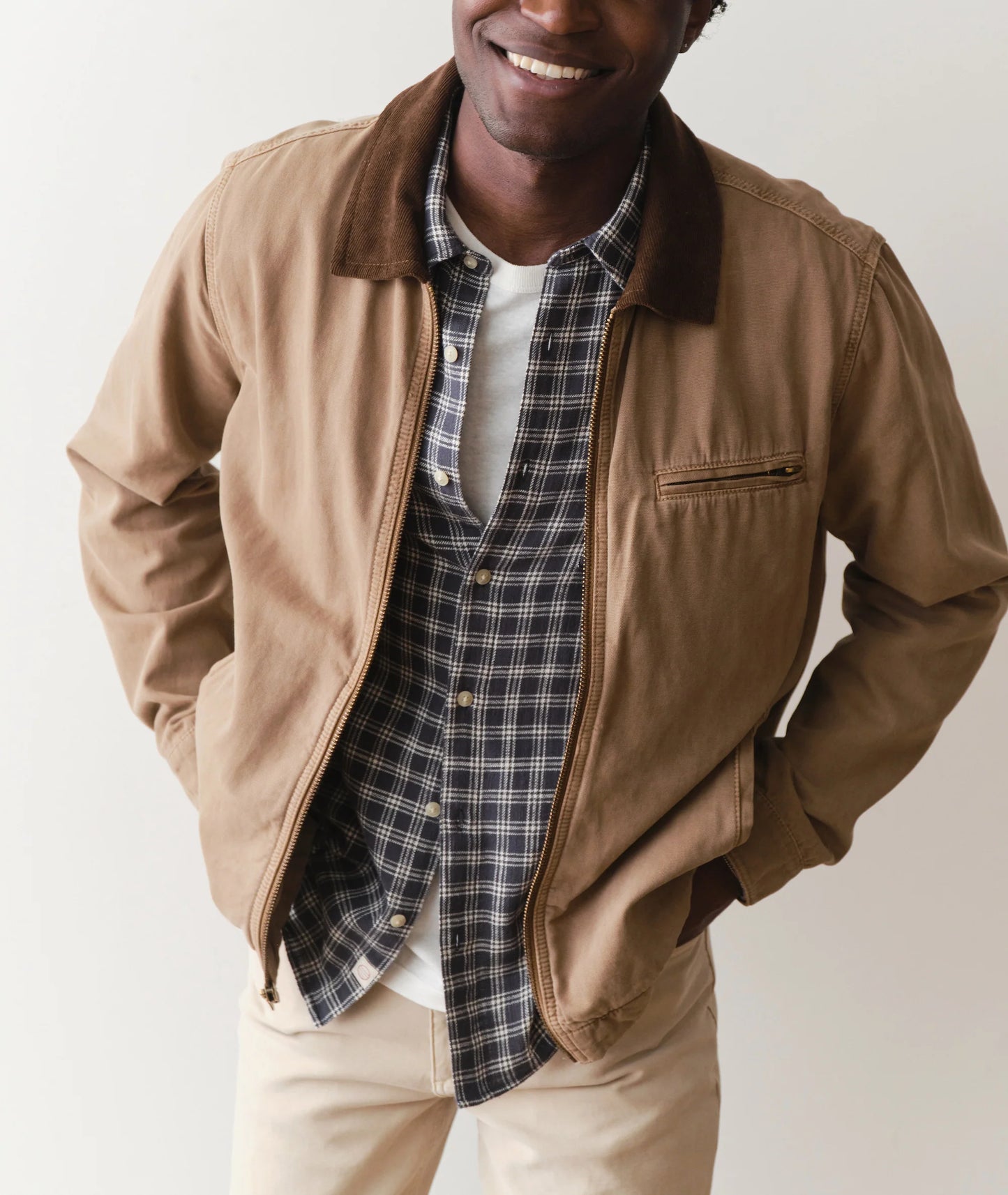 Man wearing a brown jacket over a plaid shirt with a neutral background