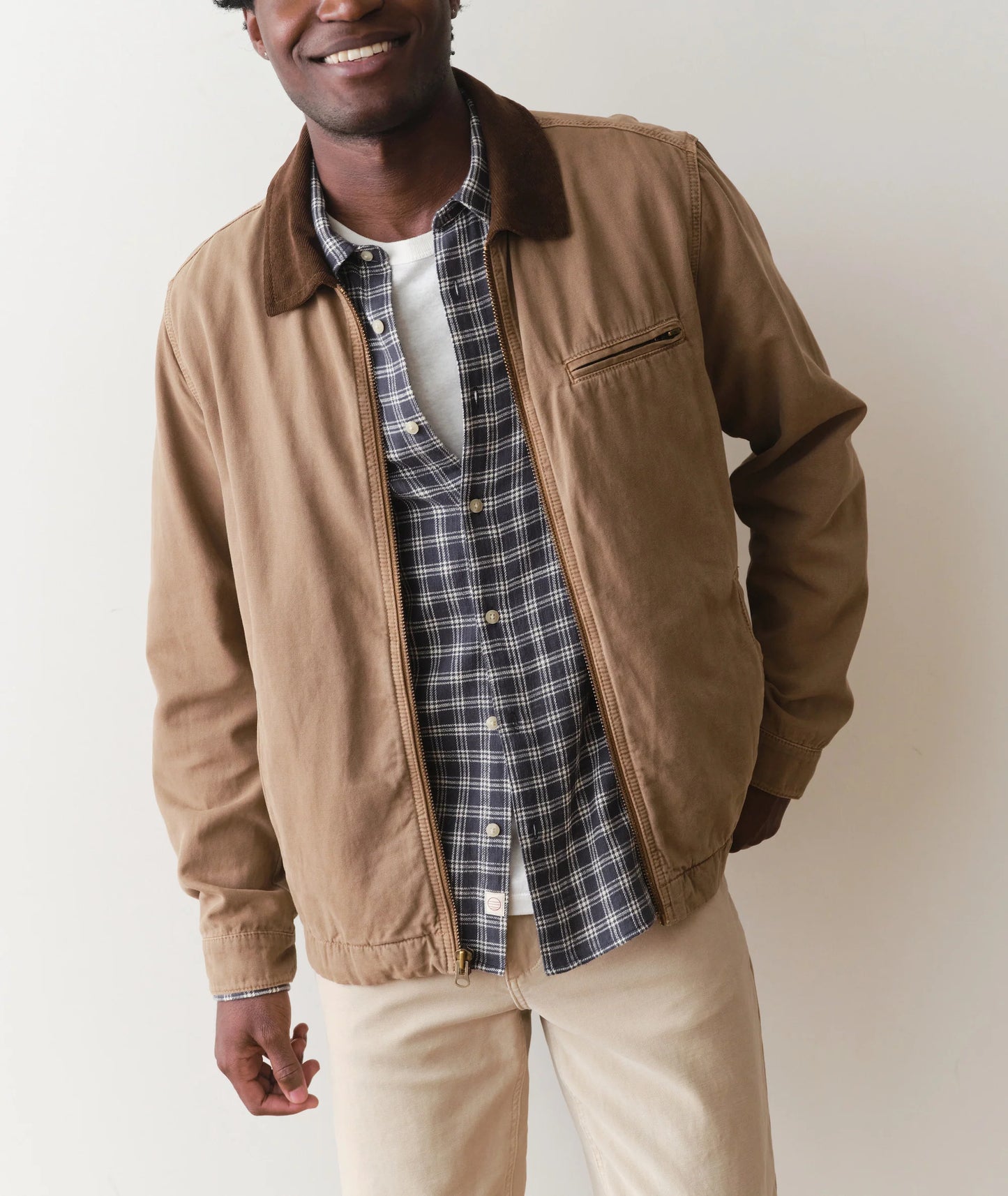 Man wearing a brown jacket over a plaid shirt with a plain background