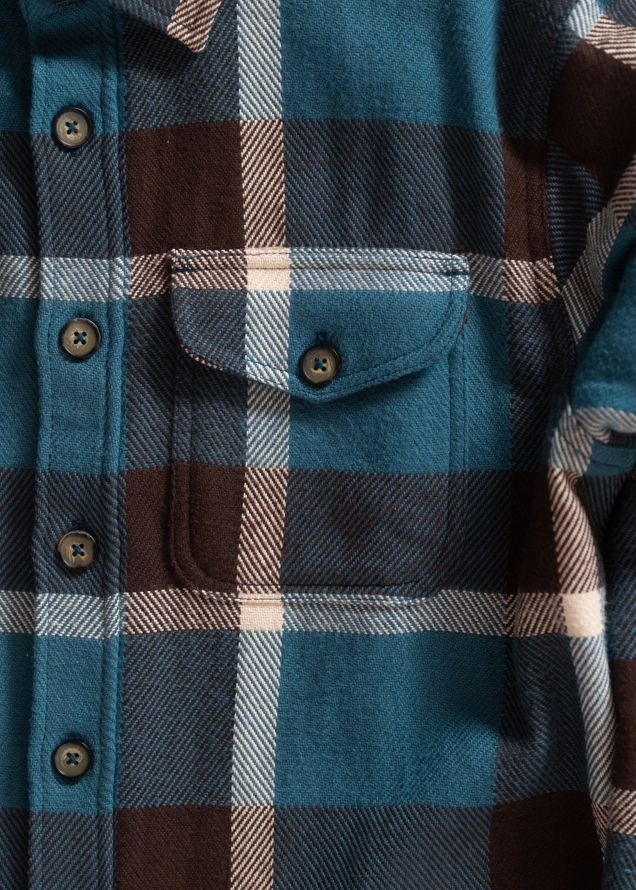 Close-up of a plaid shirt with blue, brown, and beige pattern.