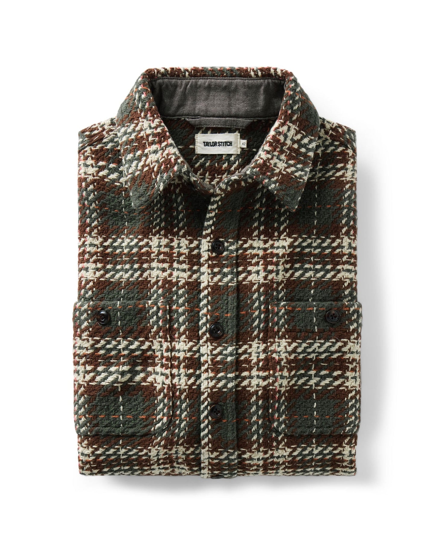 A folded plaid overshirt from Taylor Stitch, featuring a textured tweed pattern in dark green, brown, and cream. The shirt has a button-down front, a classic collar, and two buttoned chest pockets, shown against a plain white background.