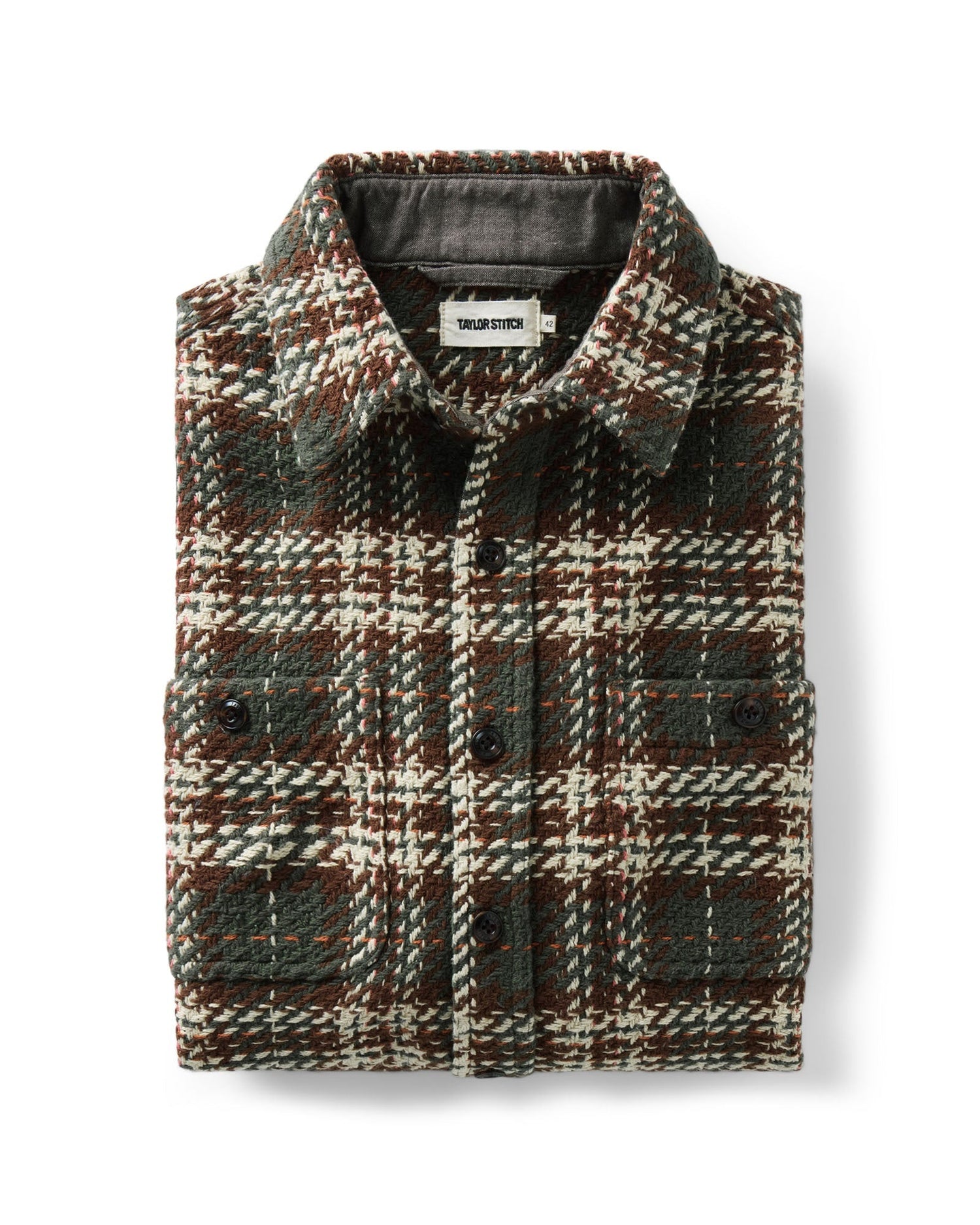 A folded plaid overshirt from Taylor Stitch, featuring a textured tweed pattern in dark green, brown, and cream. The shirt has a button-down front, a classic collar, and two buttoned chest pockets, shown against a plain white background.