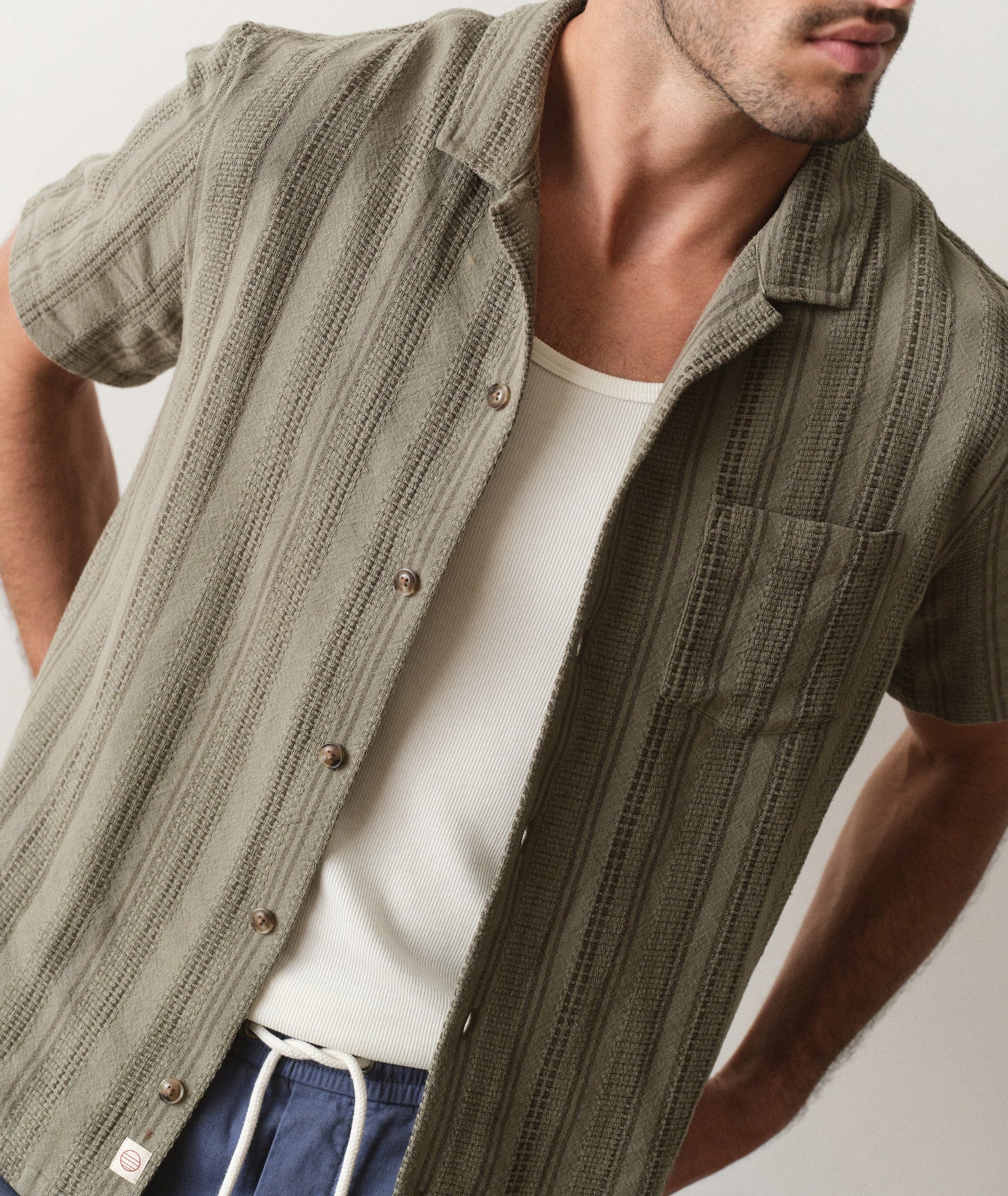 Man wearing a textured green shirt over a white tank top with a neutral background