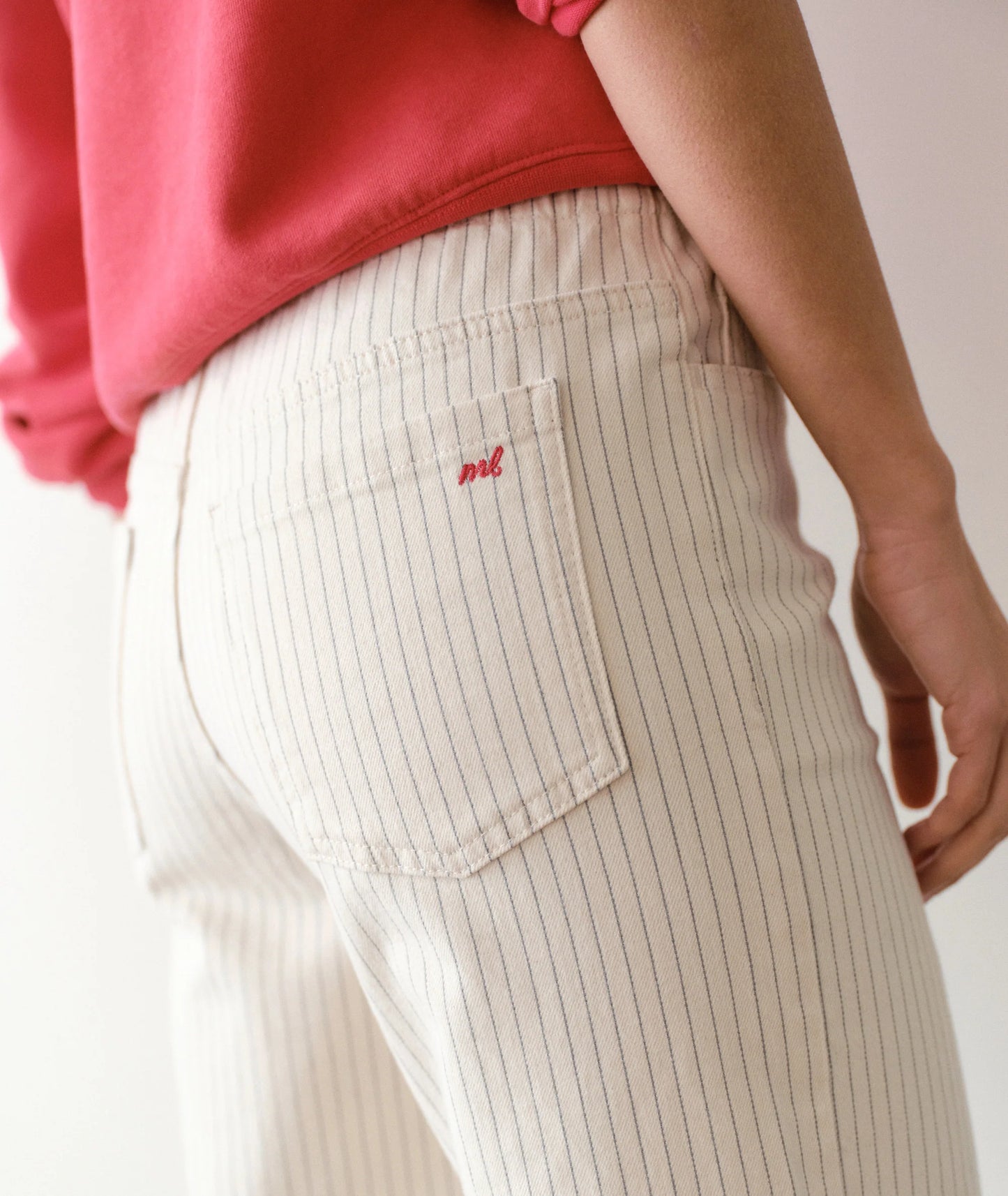 Person wearing a red top and beige striped pants with a small logo on a plain background
