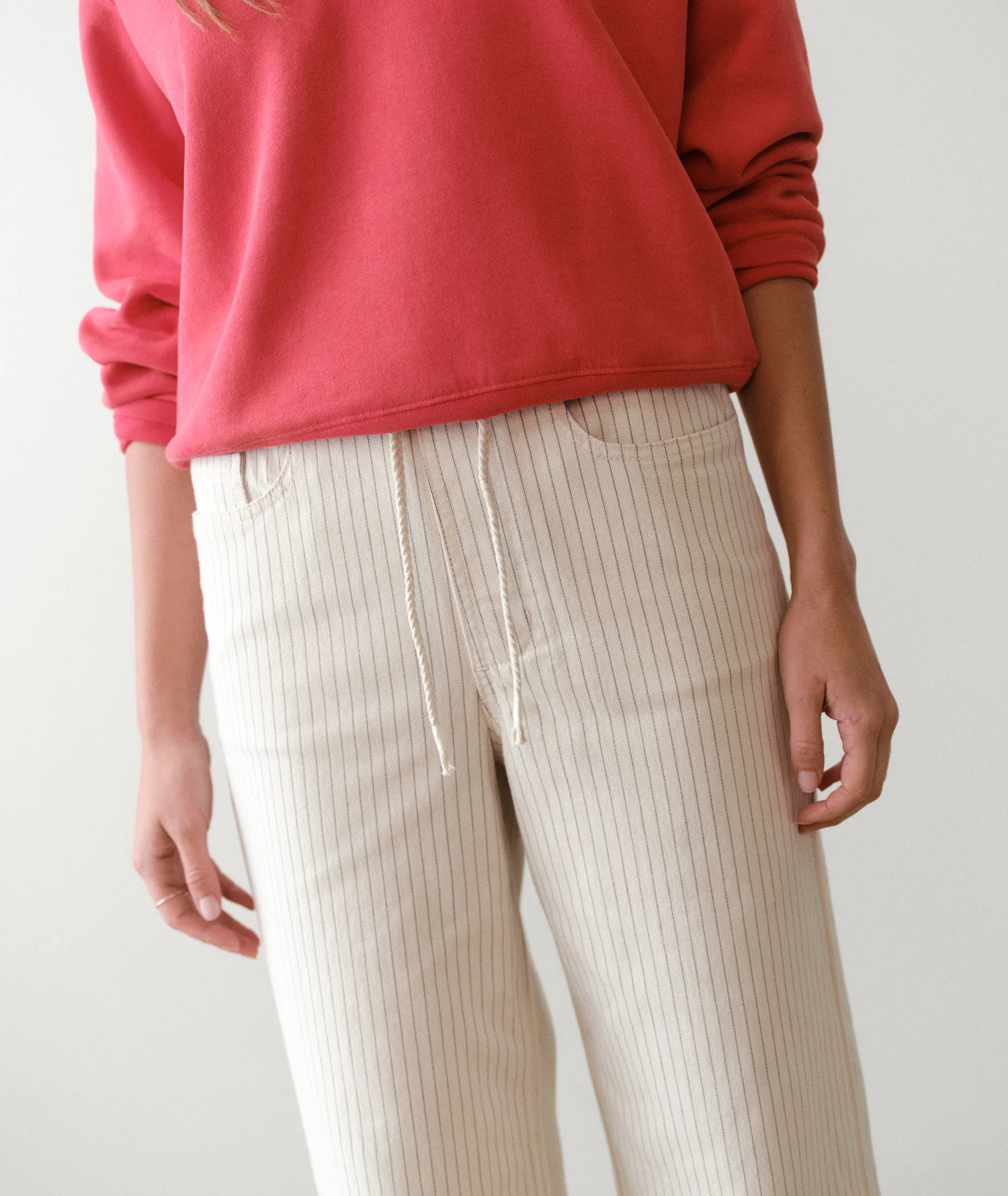 Person wearing a red sweater and beige pants on a plain background