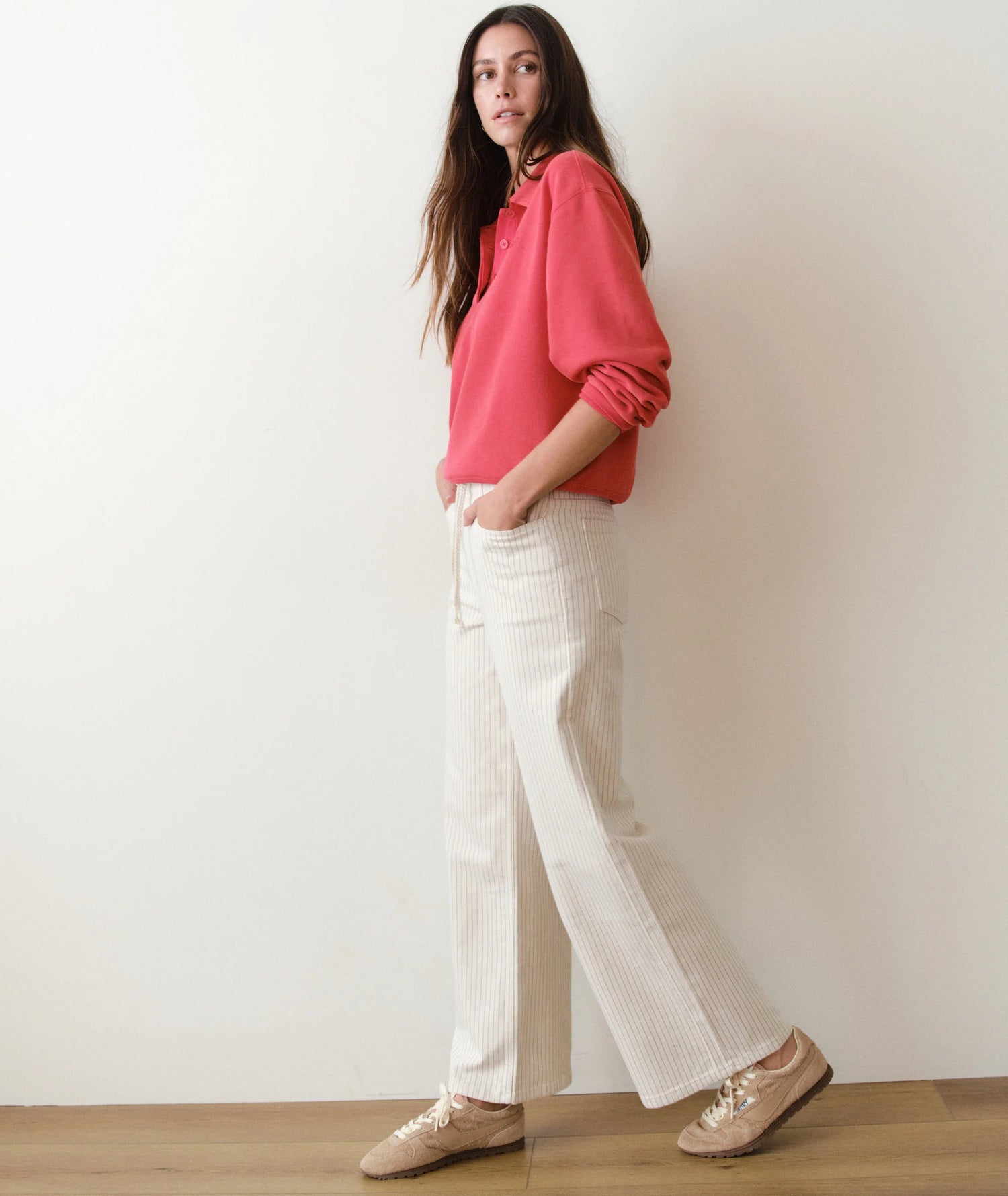 Woman wearing a red shirt and white pants against a plain background