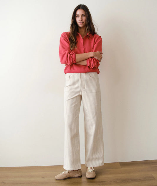 Woman wearing a red blouse and white pants against a plain background