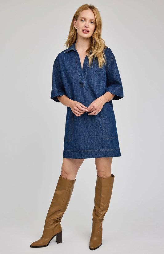 Woman wearing a blue denim dress and brown knee-high boots on a light gray background