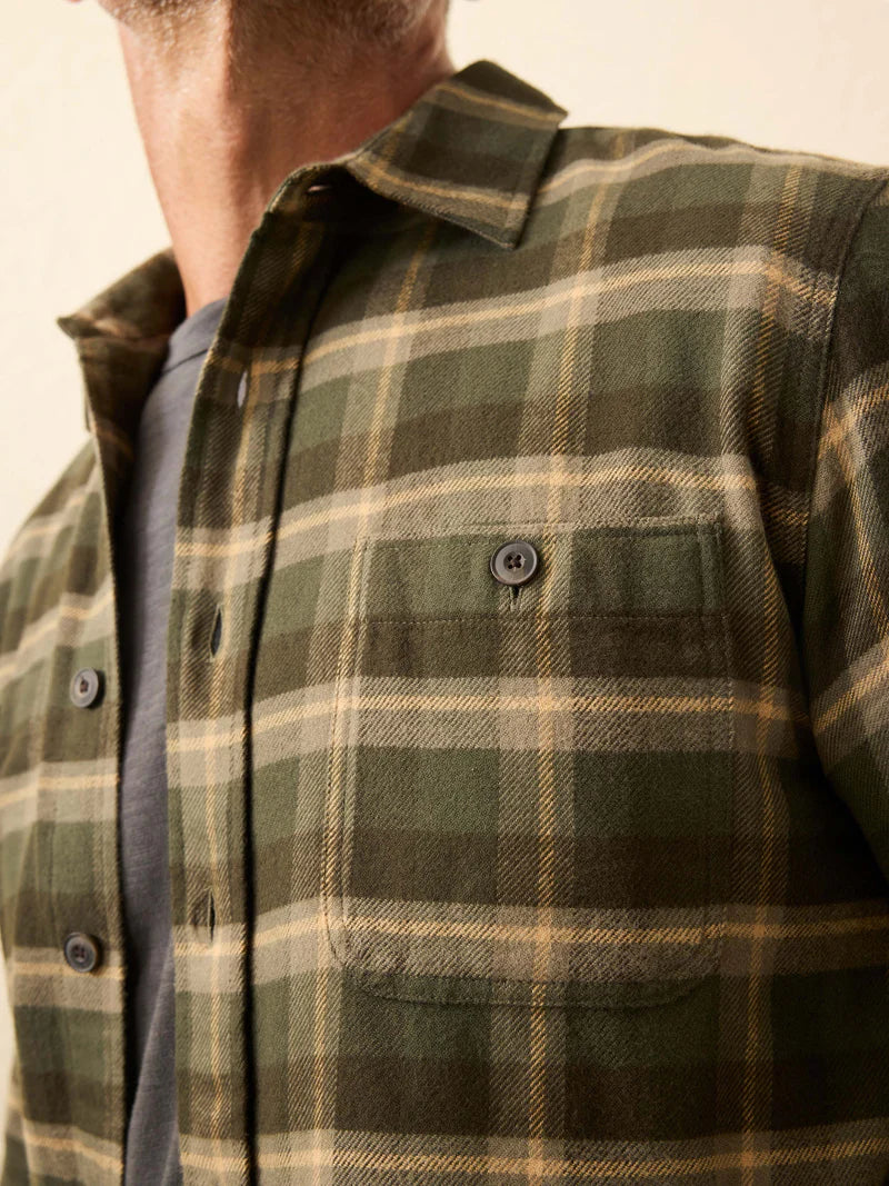 Close-up of a person wearing a green and beige plaid shirt against a neutral background