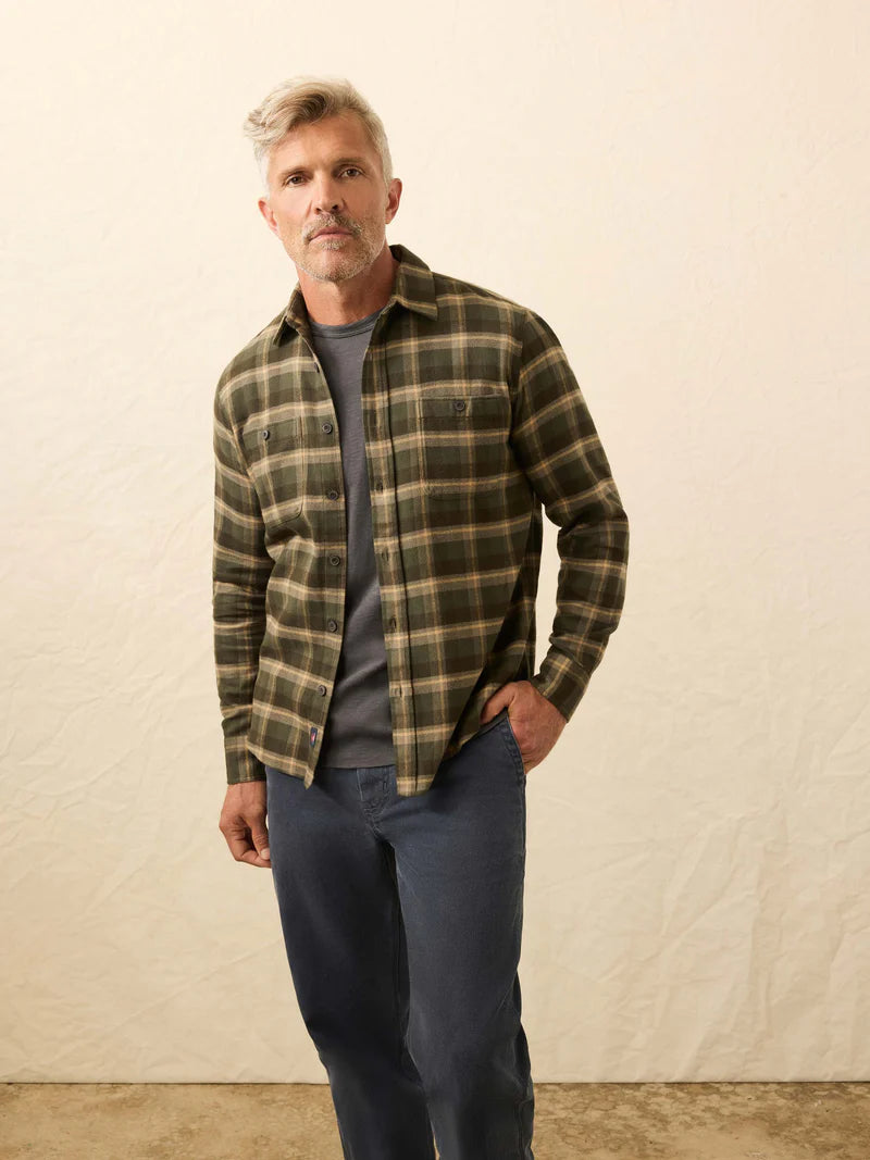 Man wearing a plaid shirt over a gray sweater and blue jeans against a beige background