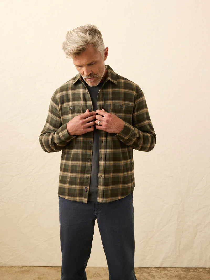 Man wearing a plaid shirt and dark pants against a plain background