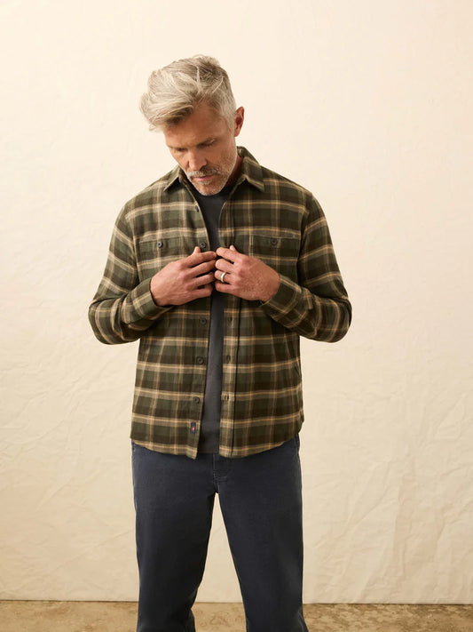 Man wearing a plaid shirt and dark pants against a plain background