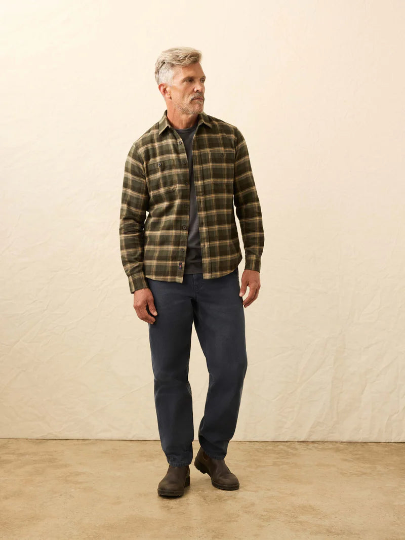 Man wearing a plaid shirt and dark pants against a beige background
