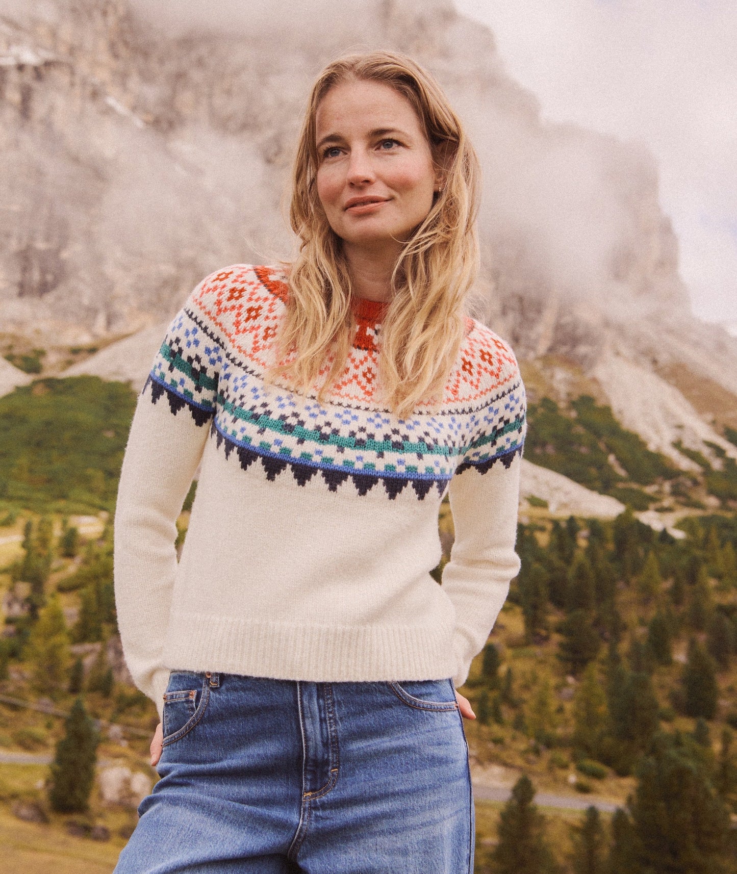 Woman wearing a patterned sweater standing in front of a mountainous landscape