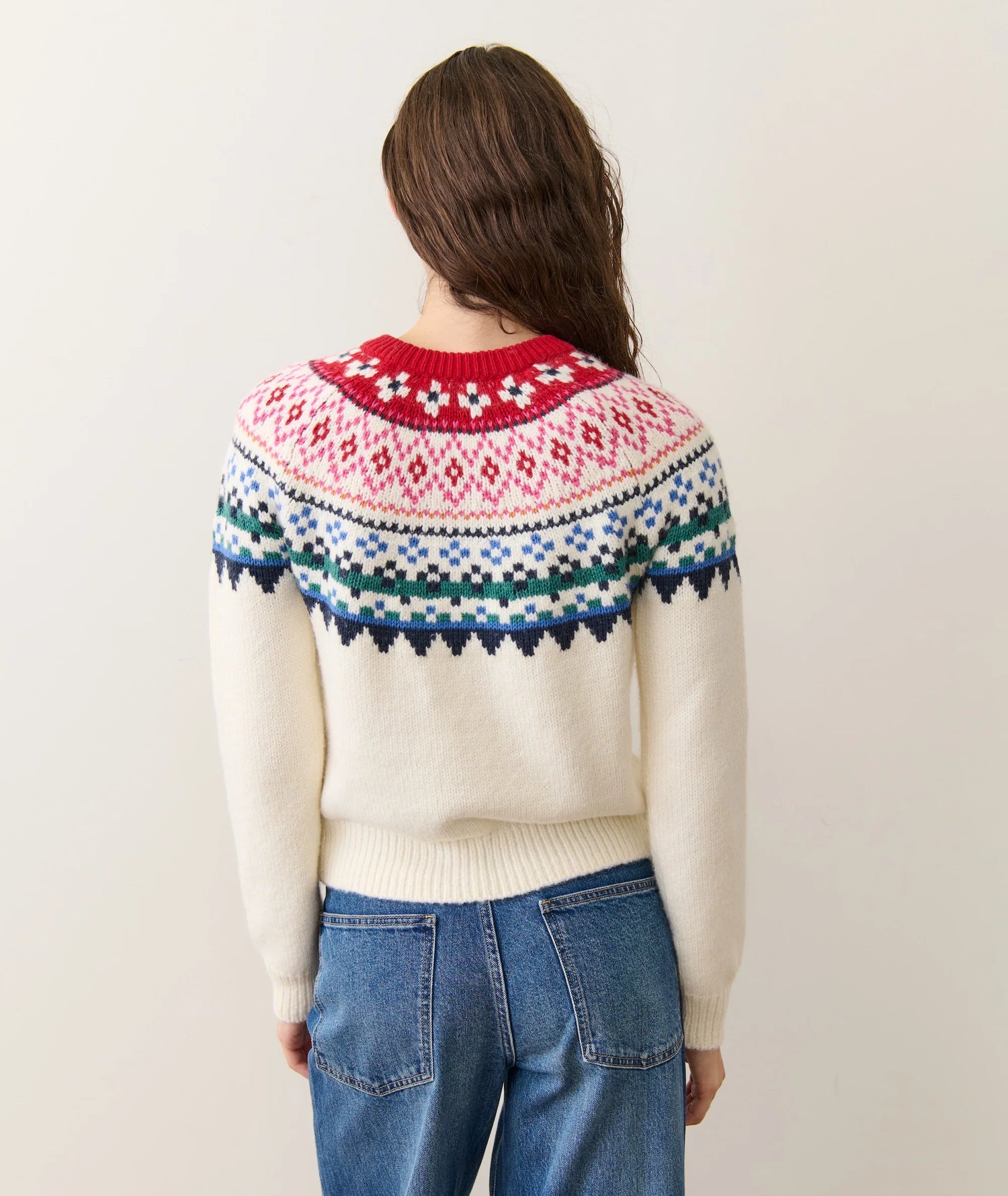 Person wearing a cream sweater with a colorful pattern on the back, standing against a plain background.