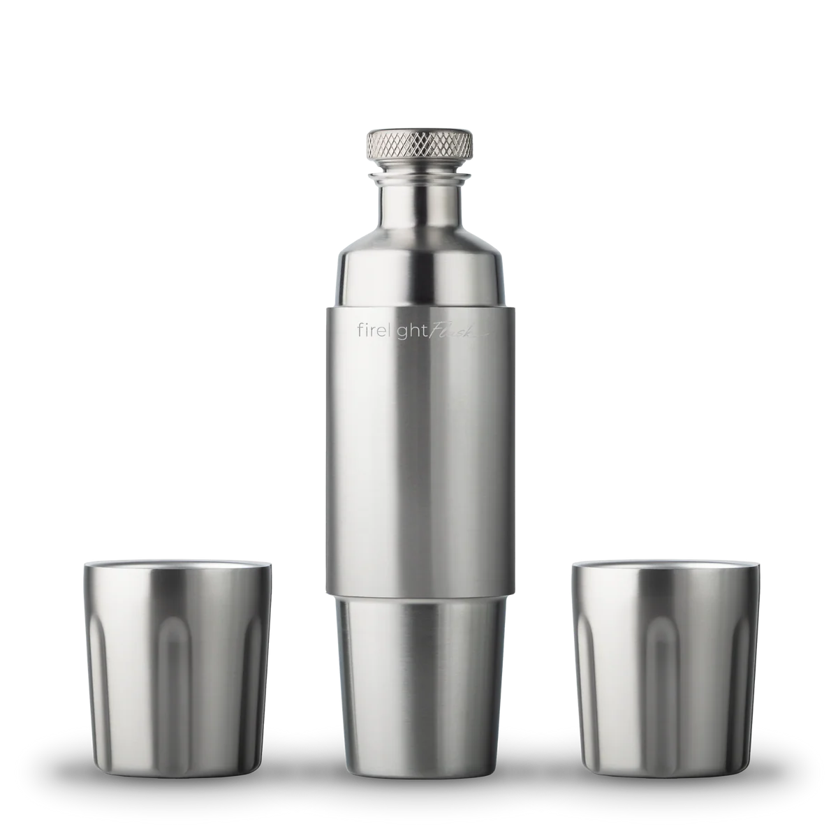 Stainless steel cocktail shaker and two matching shot glasses on a white background