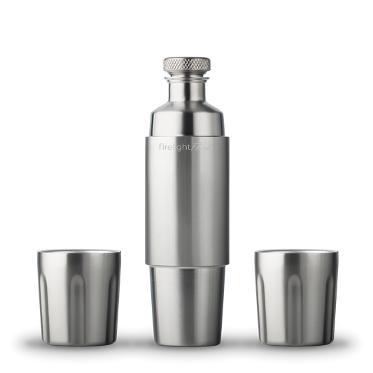 Stainless steel cocktail shaker and two matching shot glasses on a white background