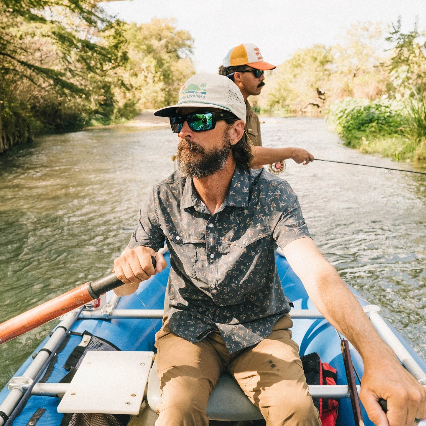 Two men in a blue raft on a river with trees lining the banks.