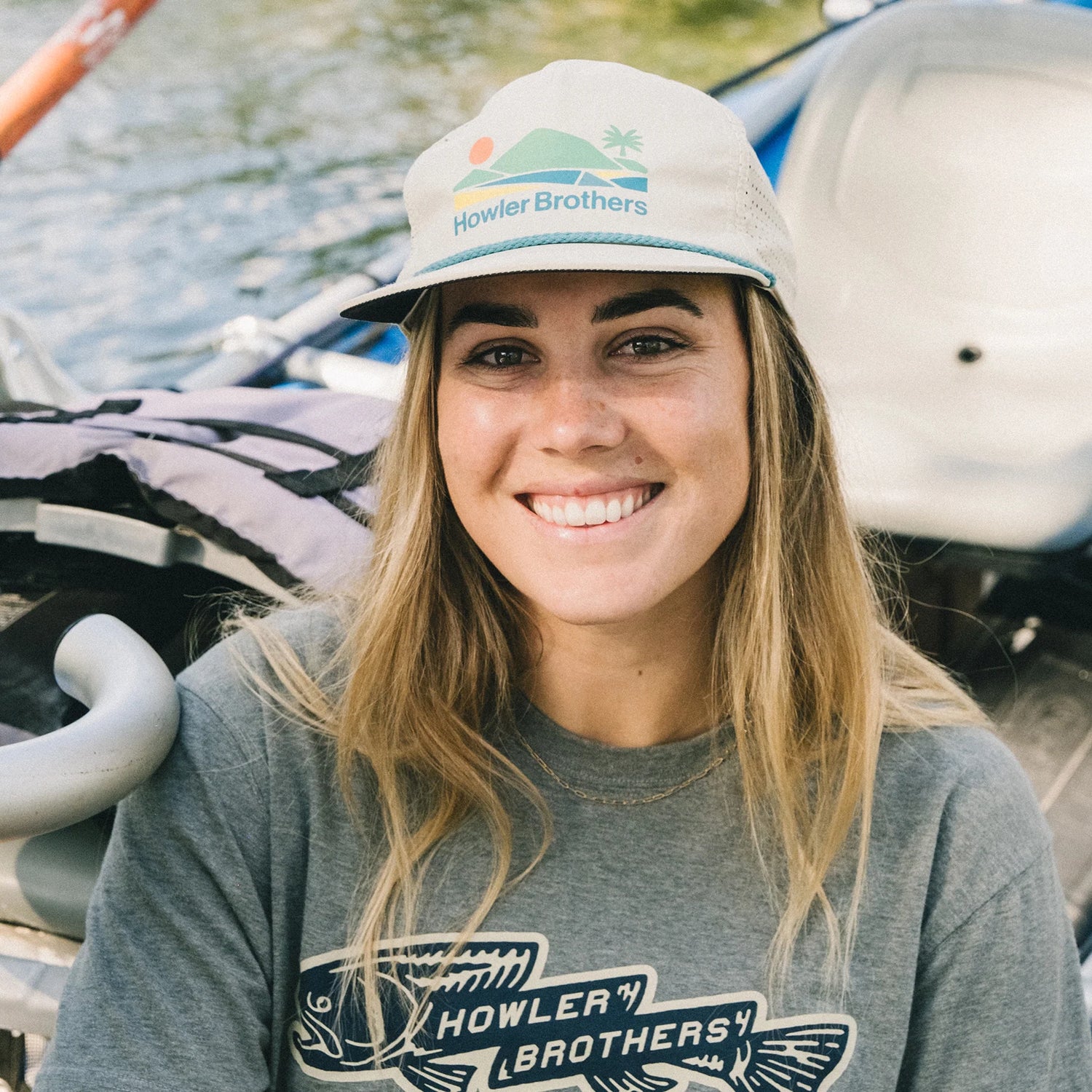 Woman wearing a Howler Brothers cap and shirt with kayaks in the background