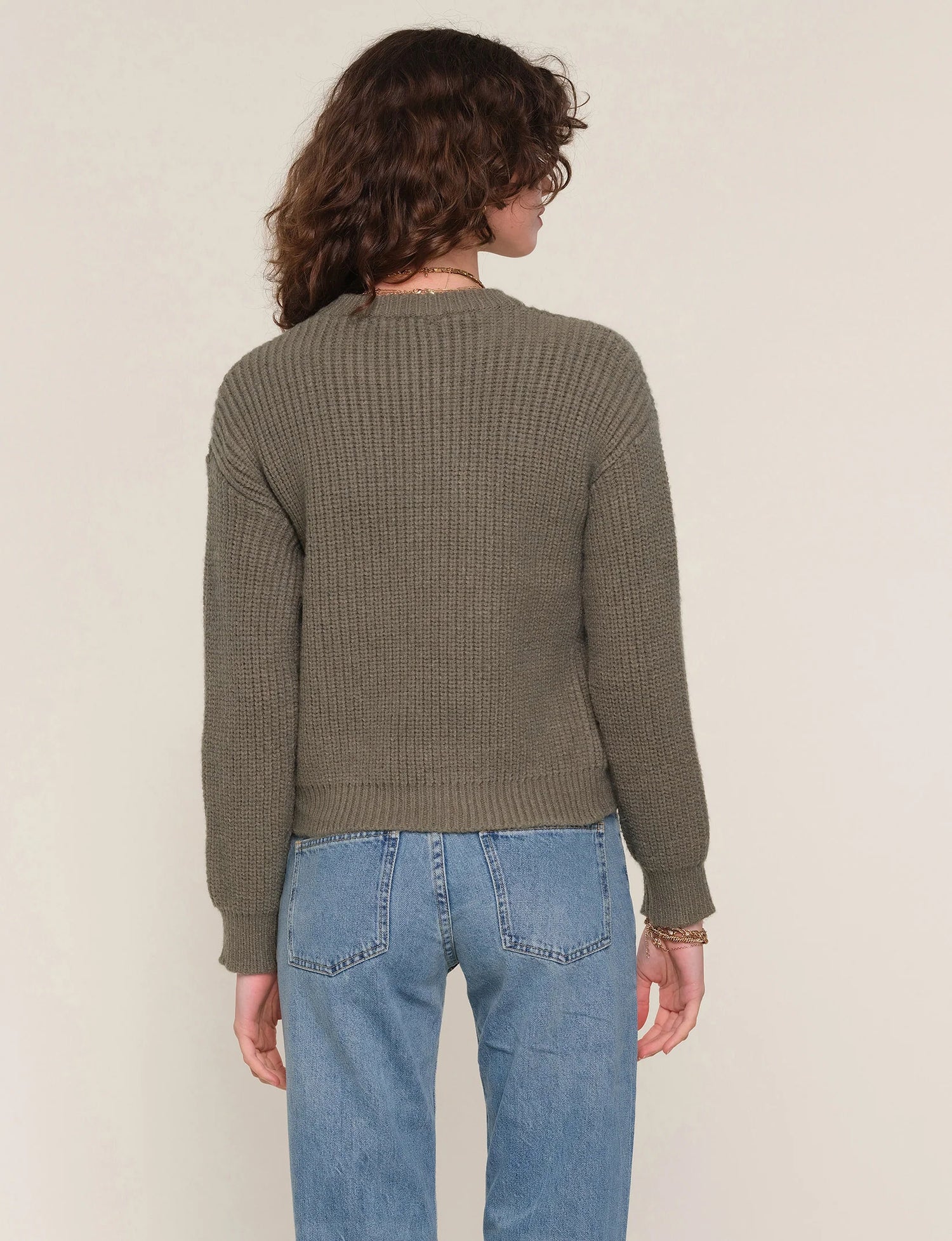 Person wearing a green sweater and blue jeans against a beige background