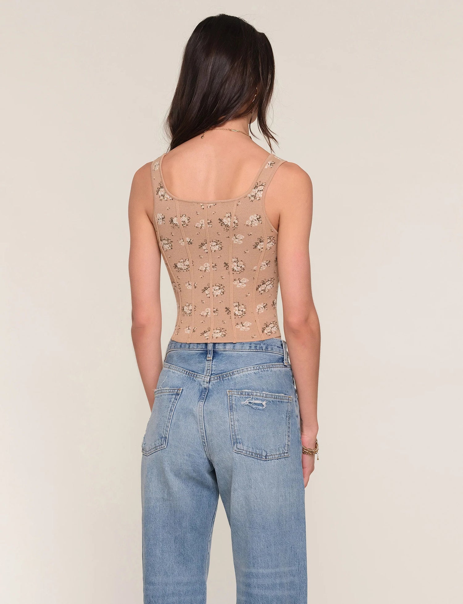 Woman wearing a patterned tank top and blue jeans on a beige background