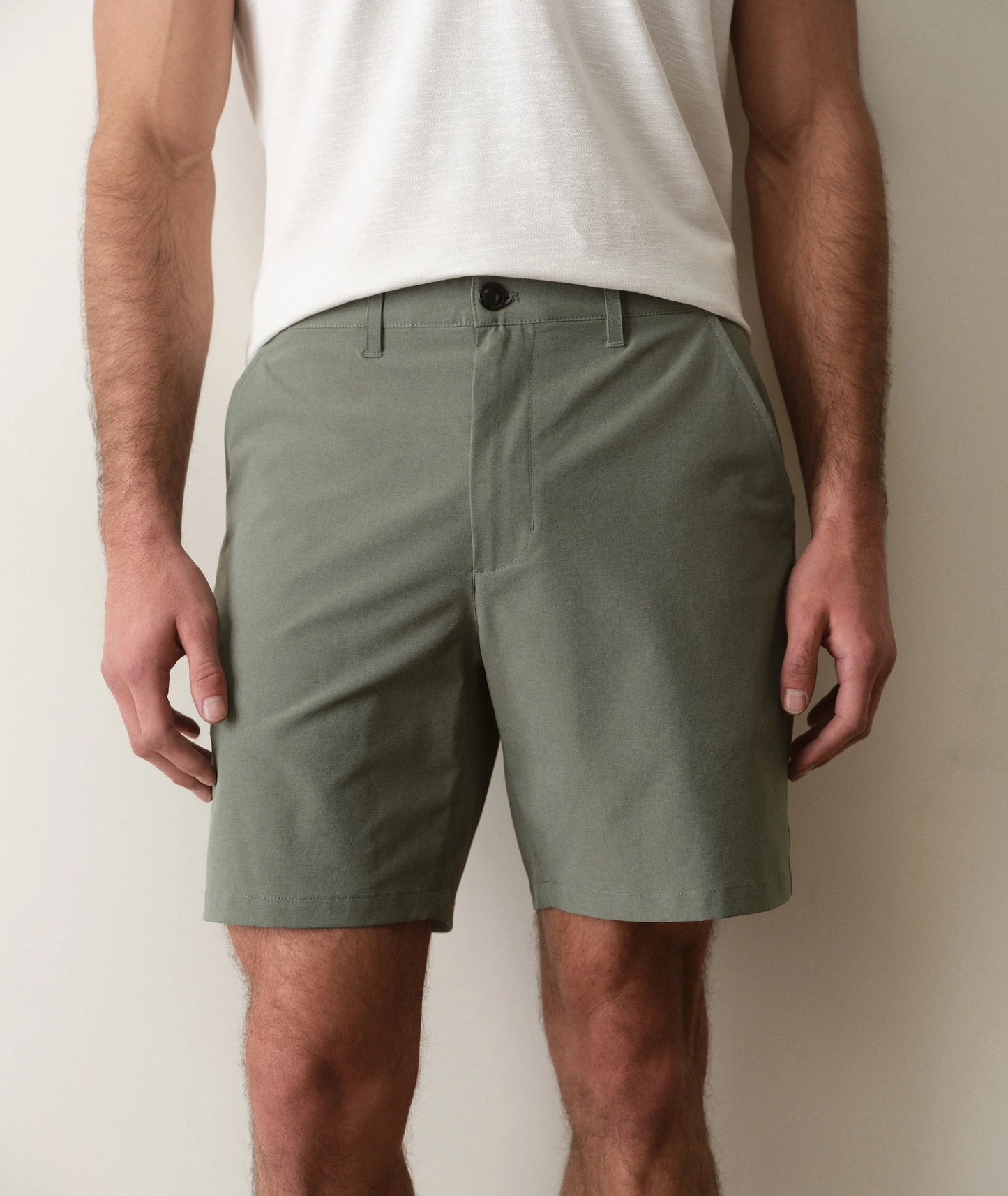 Person wearing olive green shorts and a white shirt against a plain background