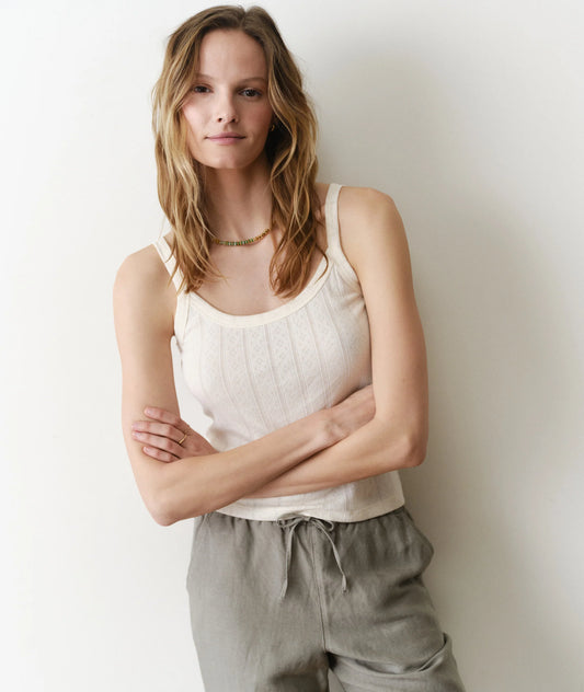 Woman wearing a white tank top and gray pants against a plain background