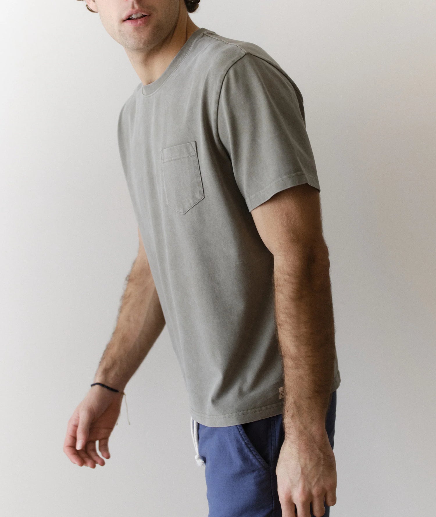 Man wearing a green t-shirt and blue pants against a plain background