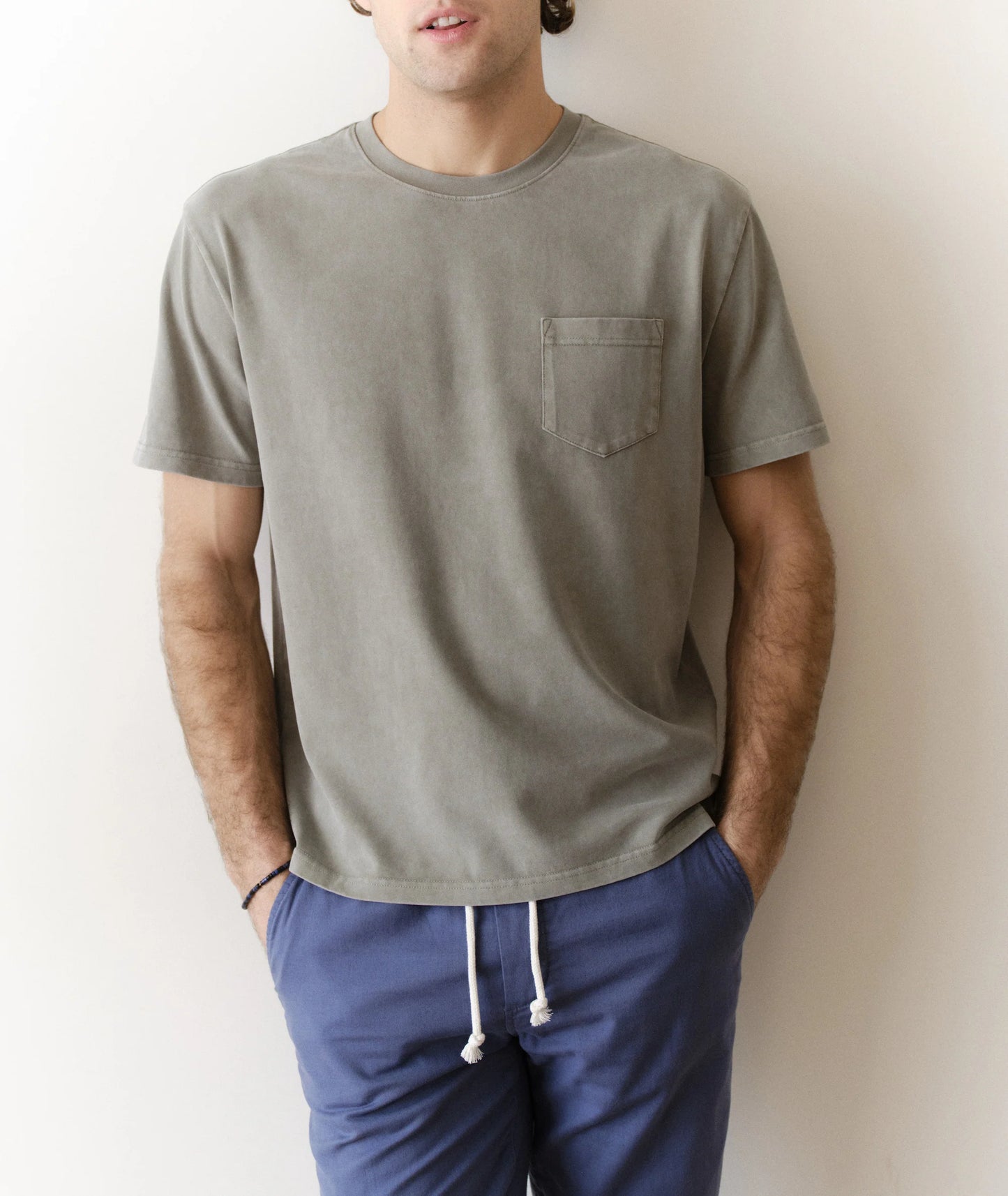 Person wearing a green t-shirt with a pocket and blue pants against a plain background